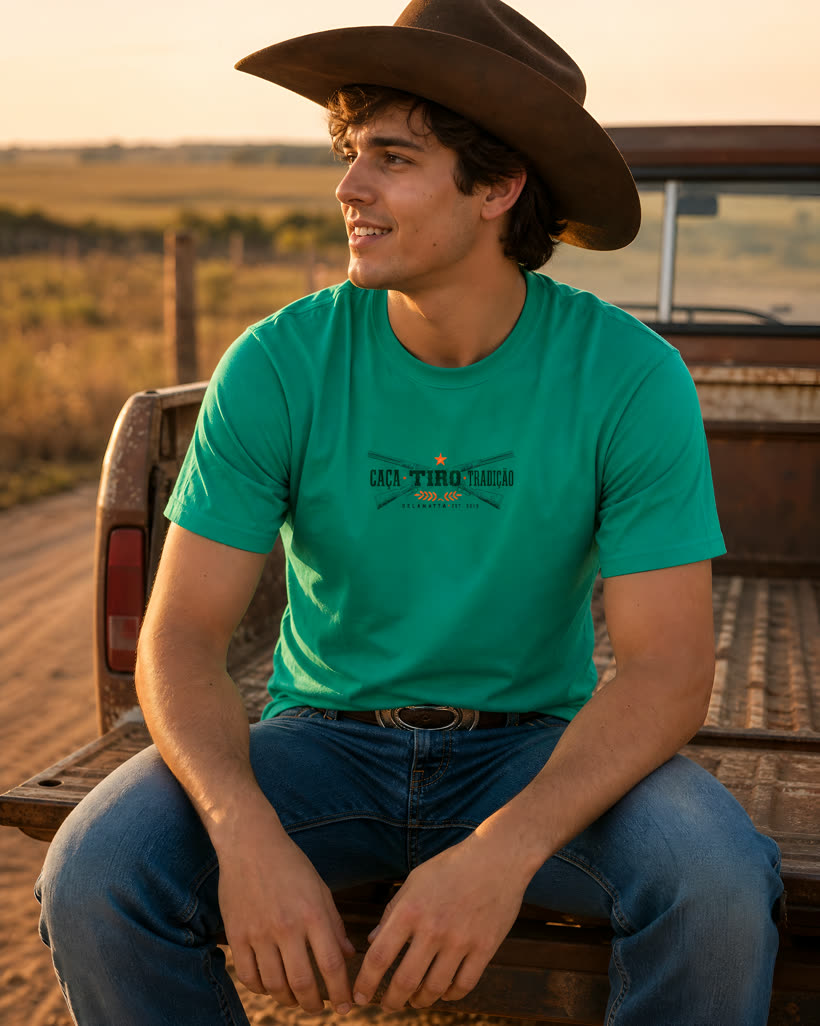Homem de chapéu vestindo a camiseta verde Caça Tiro Tradição na caçamba da caminhonete